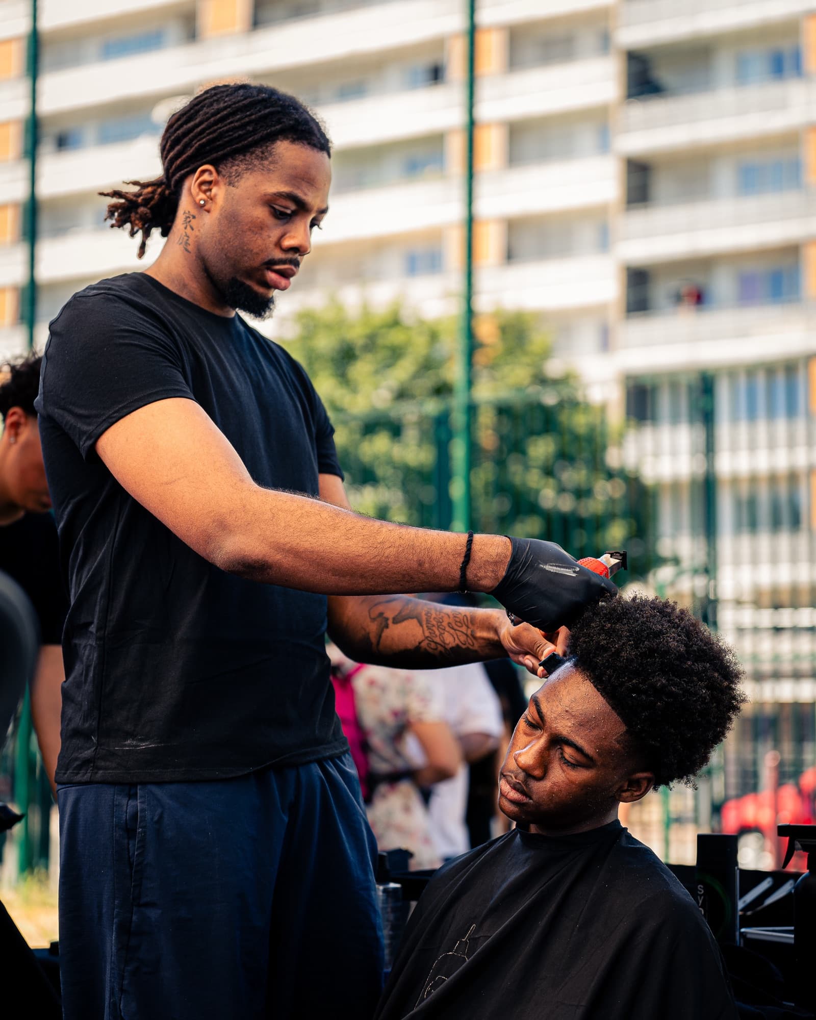 Un barbier coupe les cheveux d’un jeune au bord du terrain, l’une des animations de la block party BUCKET