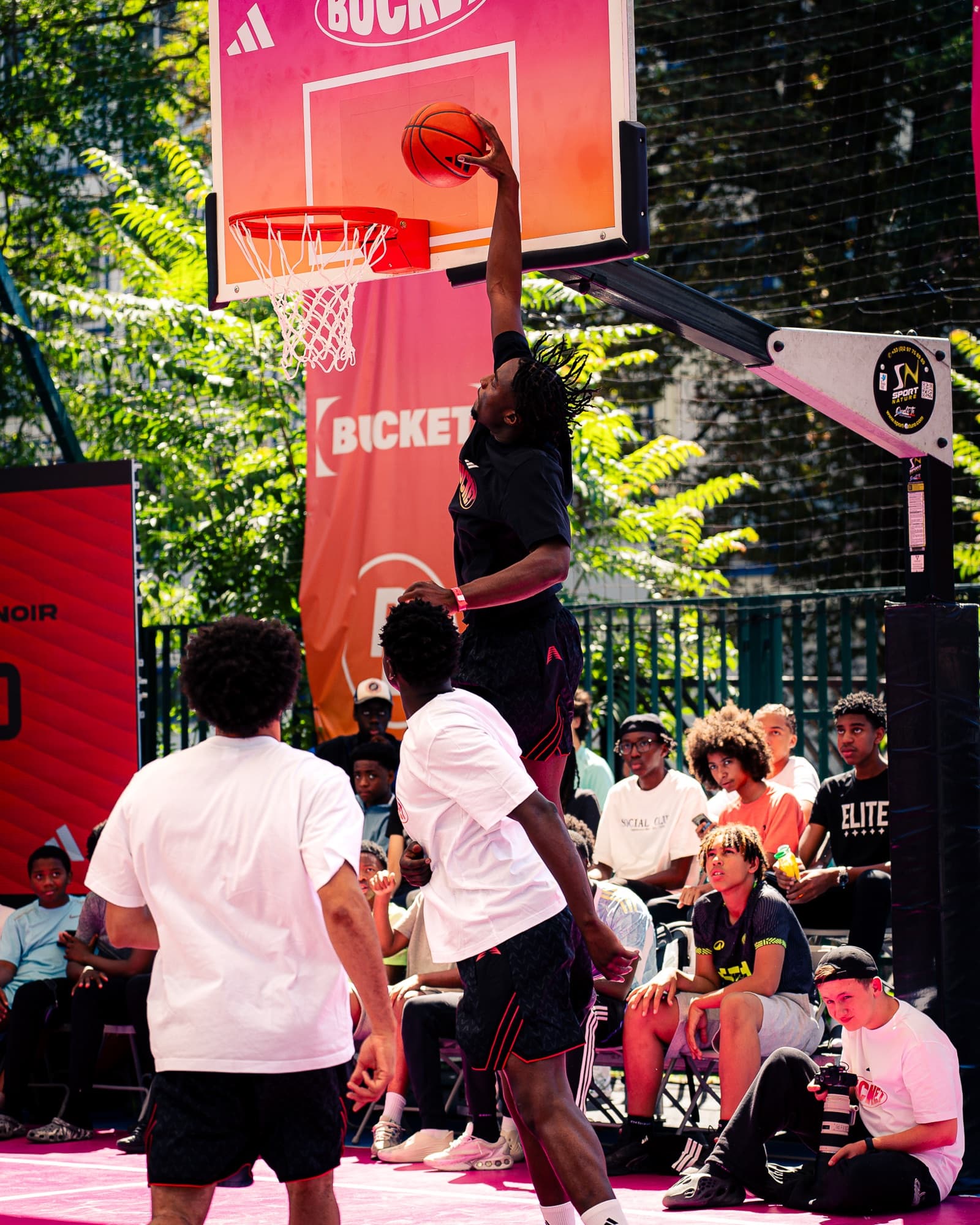 Dunk à deux mains au cercle devant les bâches adidas × BUCKET, public assis tout autour du terrain