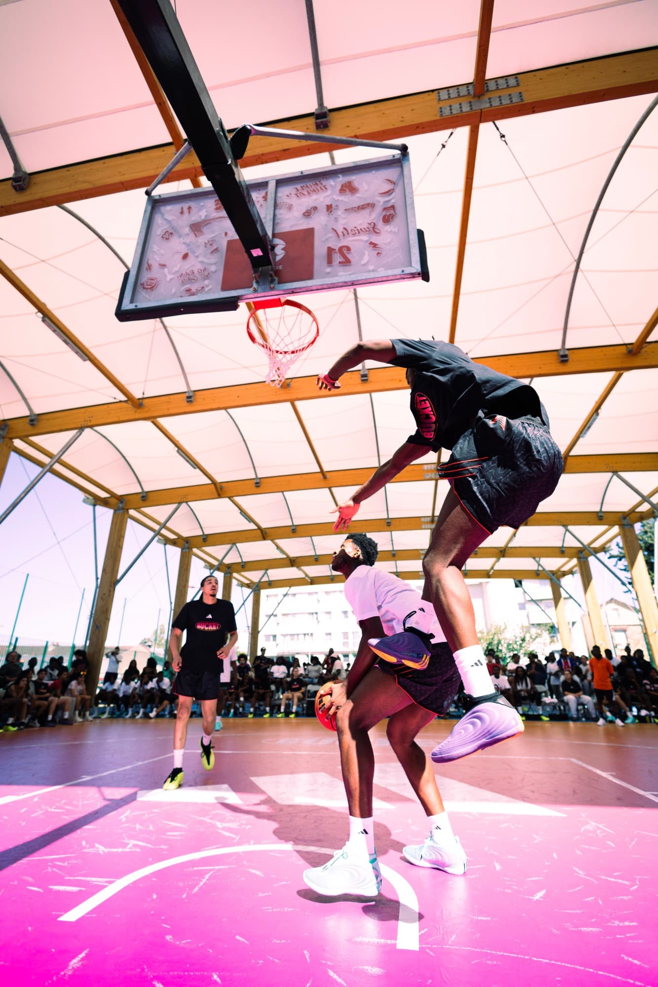 Dunk sous la halle pendant le tournoi 3v3 BUCKET, le joueur en plein vol au-dessus de son adversaire