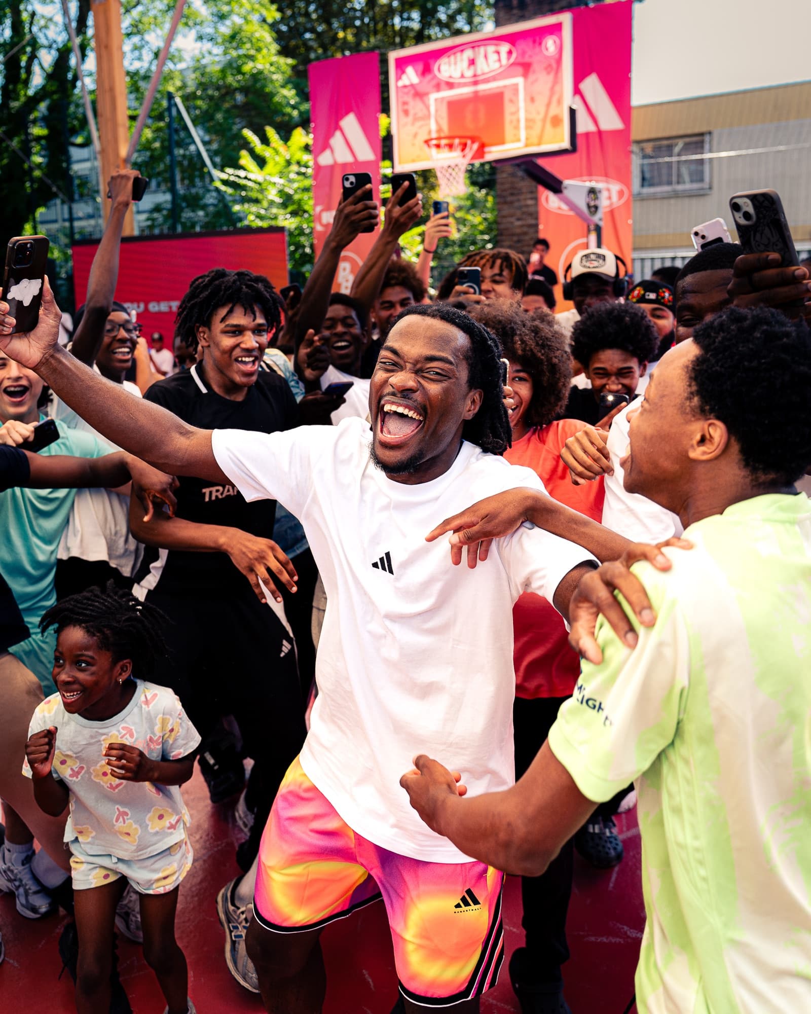 La foule en folie autour d’un joueur, bras levés et téléphones sortis, devant le panneau BUCKET × adidas
