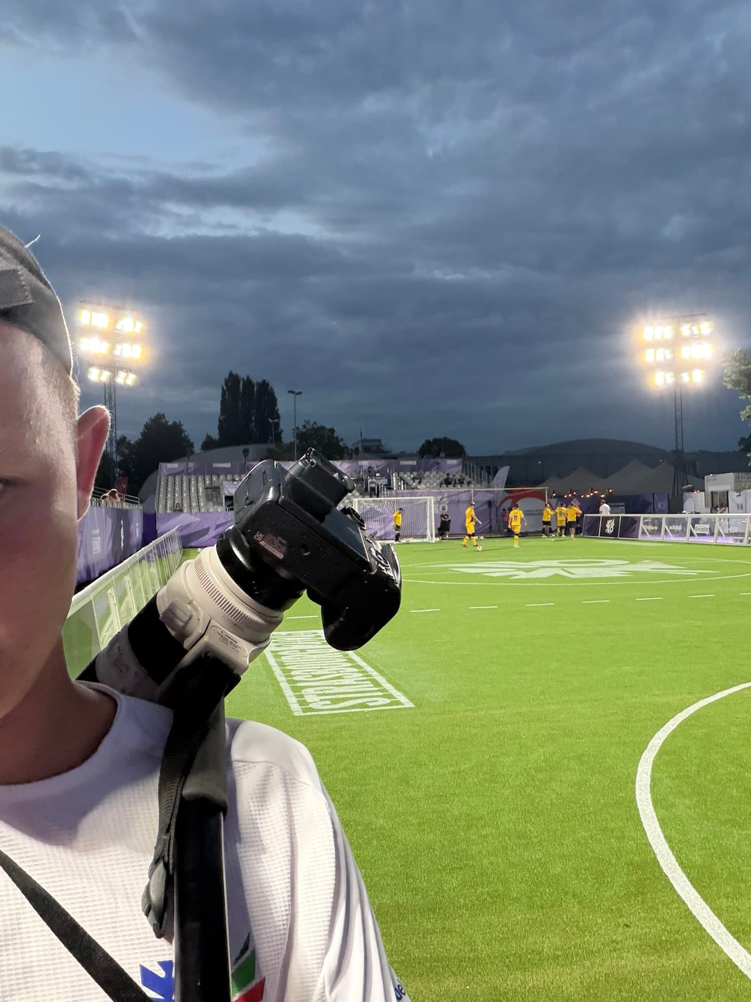 Un photographe de la compétition au bord du terrain, appareil photo au poing, de nuit sous les projecteurs