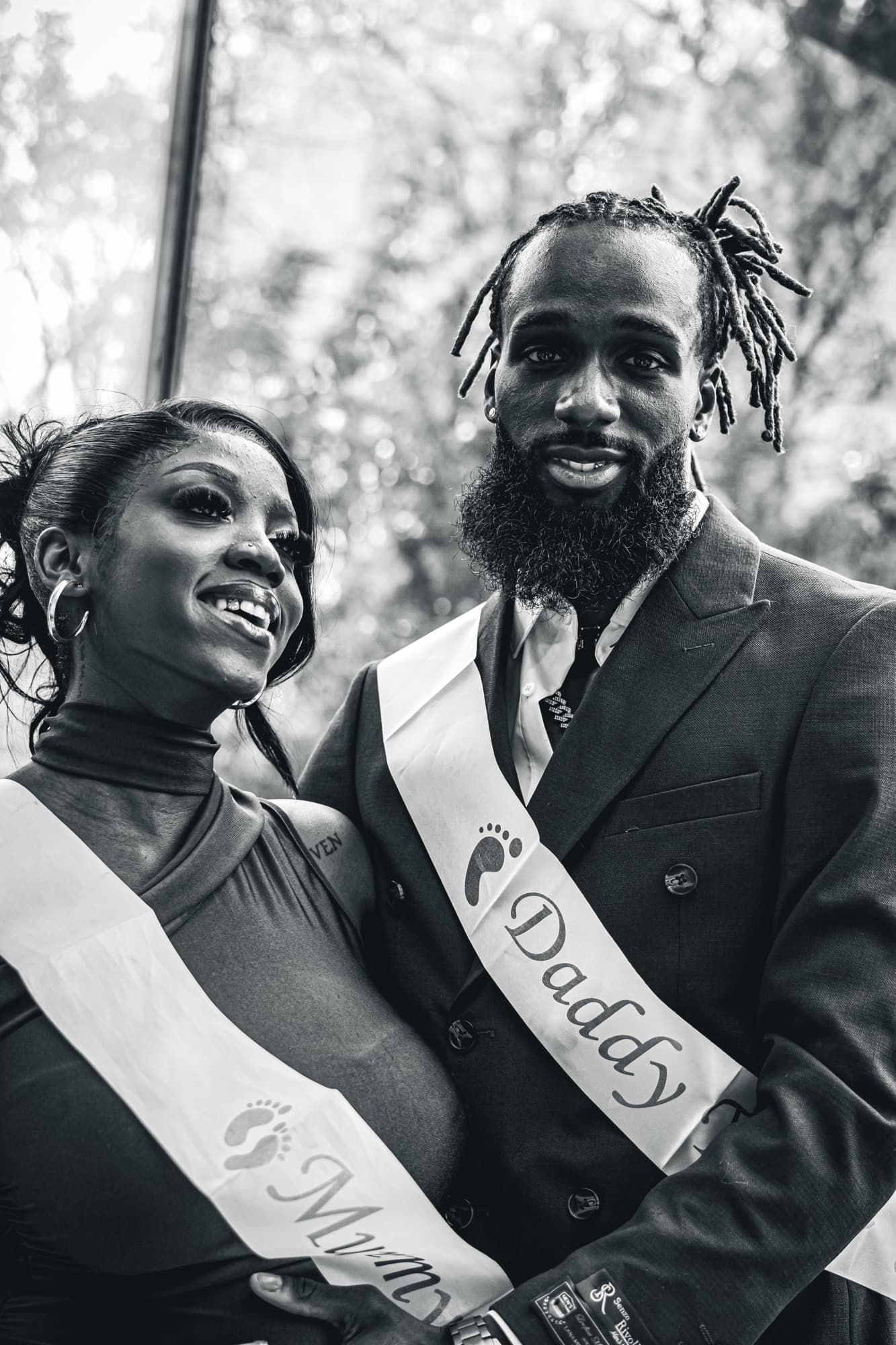 Portrait en noir et blanc du couple, l’écharpe « Daddy to be » sur le costume