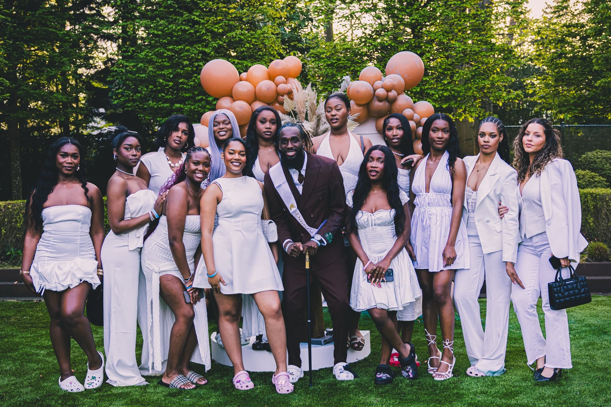 Photo de groupe de tous les invités habillés en blanc, dans le jardin, devant les ballons