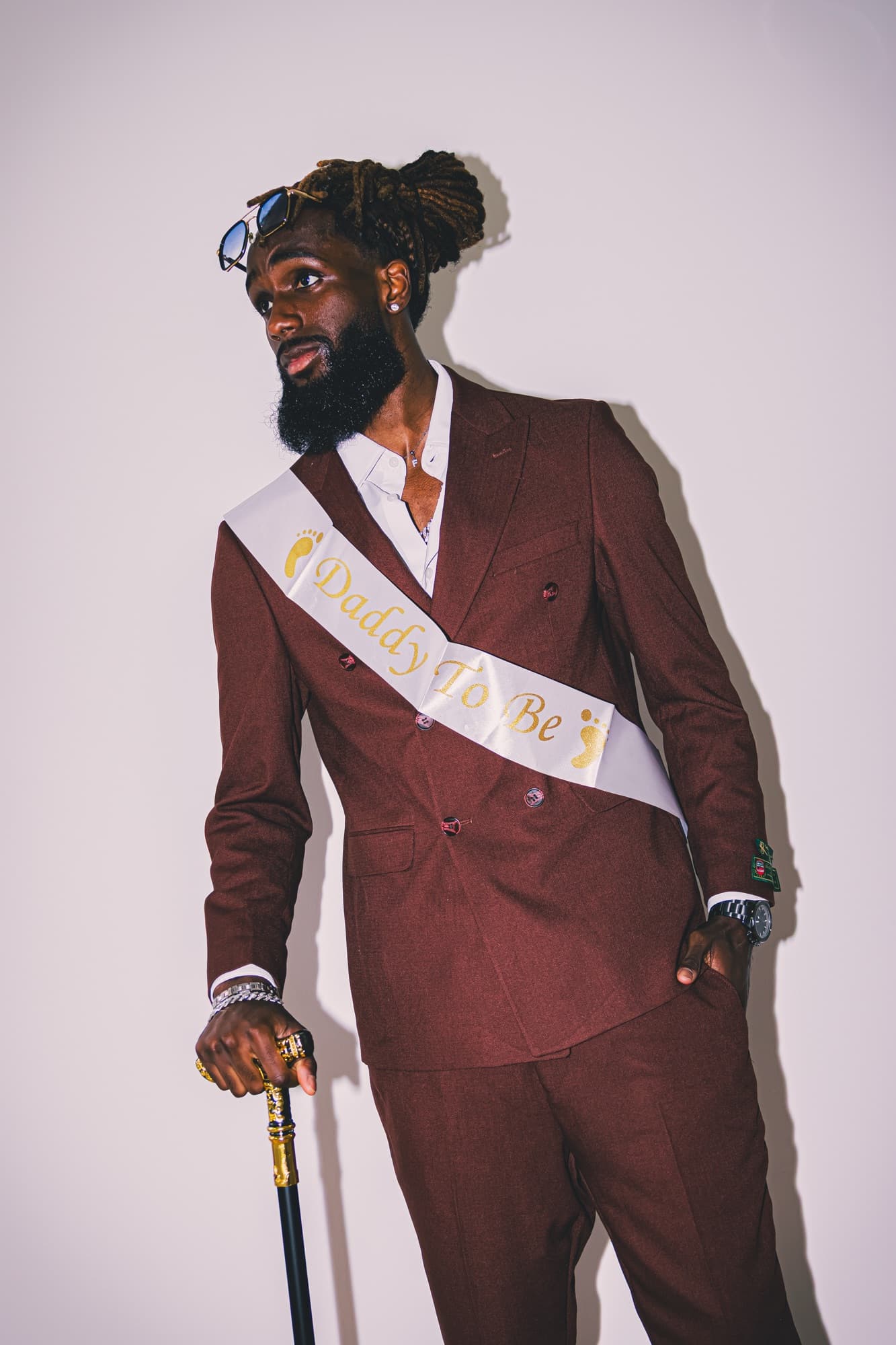 Le futur papa pose en costume bordeaux et canne, dans la maison, avant la fête