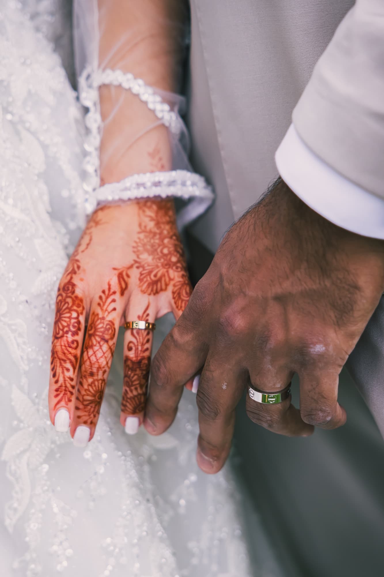 Les mains des mariés avec le henné et les alliances, en noir et blanc, sur la dentelle de la robe
