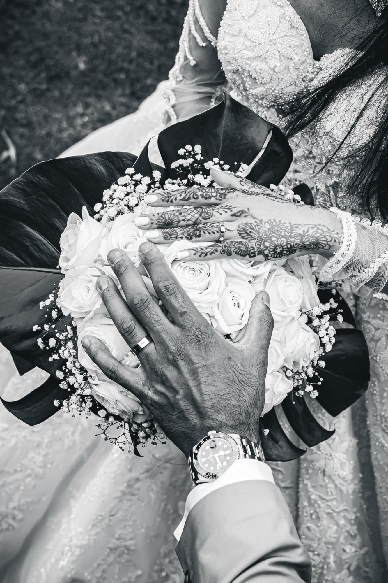 Le bouquet de roses blanches tenu par les mains des mariés, vu du dessus, en noir et blanc