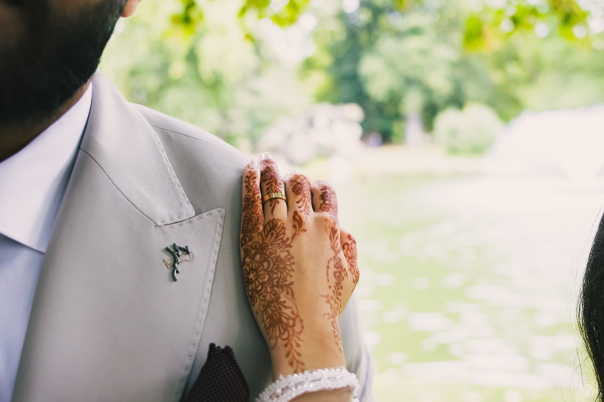 La main de la mariée décorée de henné posée sur le revers du costume du marié, dans le parc