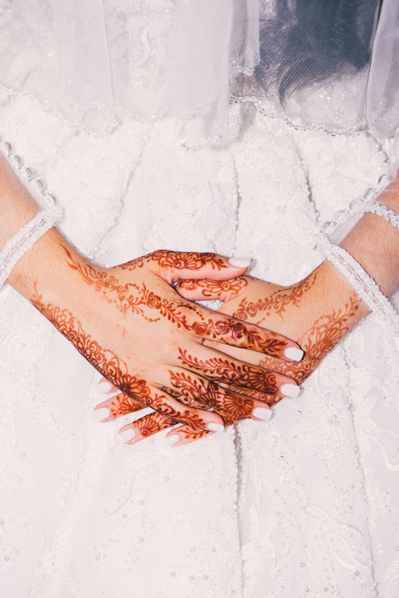 Les mains de la mariée décorées de henné rouge, posées sur sa robe de mariée blanche brodée