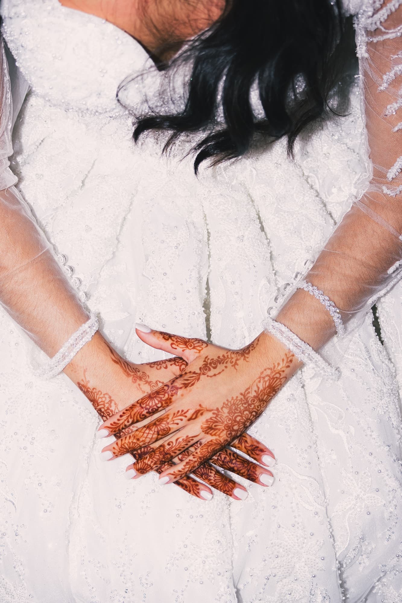 Les mains de la mariée croisées sur sa robe blanche, le henné et un bracelet de perles