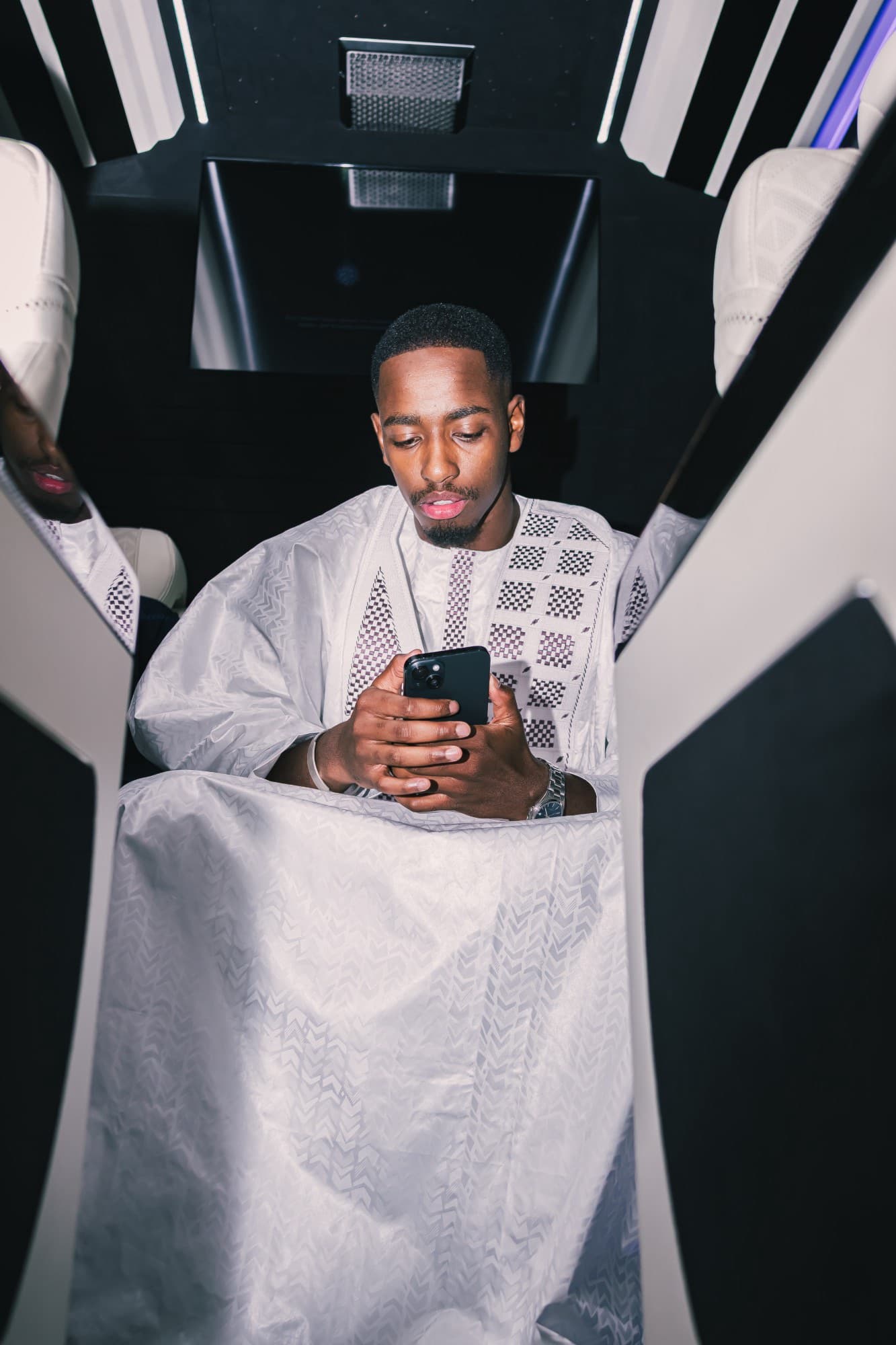 Le marié en tenue blanche brodée assis dans un minibus de prestige, son téléphone dans les mains