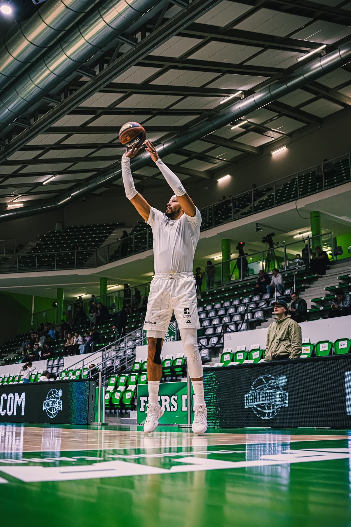 Un joueur d’ASVEL en blanc tire à l’échauffement sous les projecteurs de la salle, avant le match contre Nanterre 92