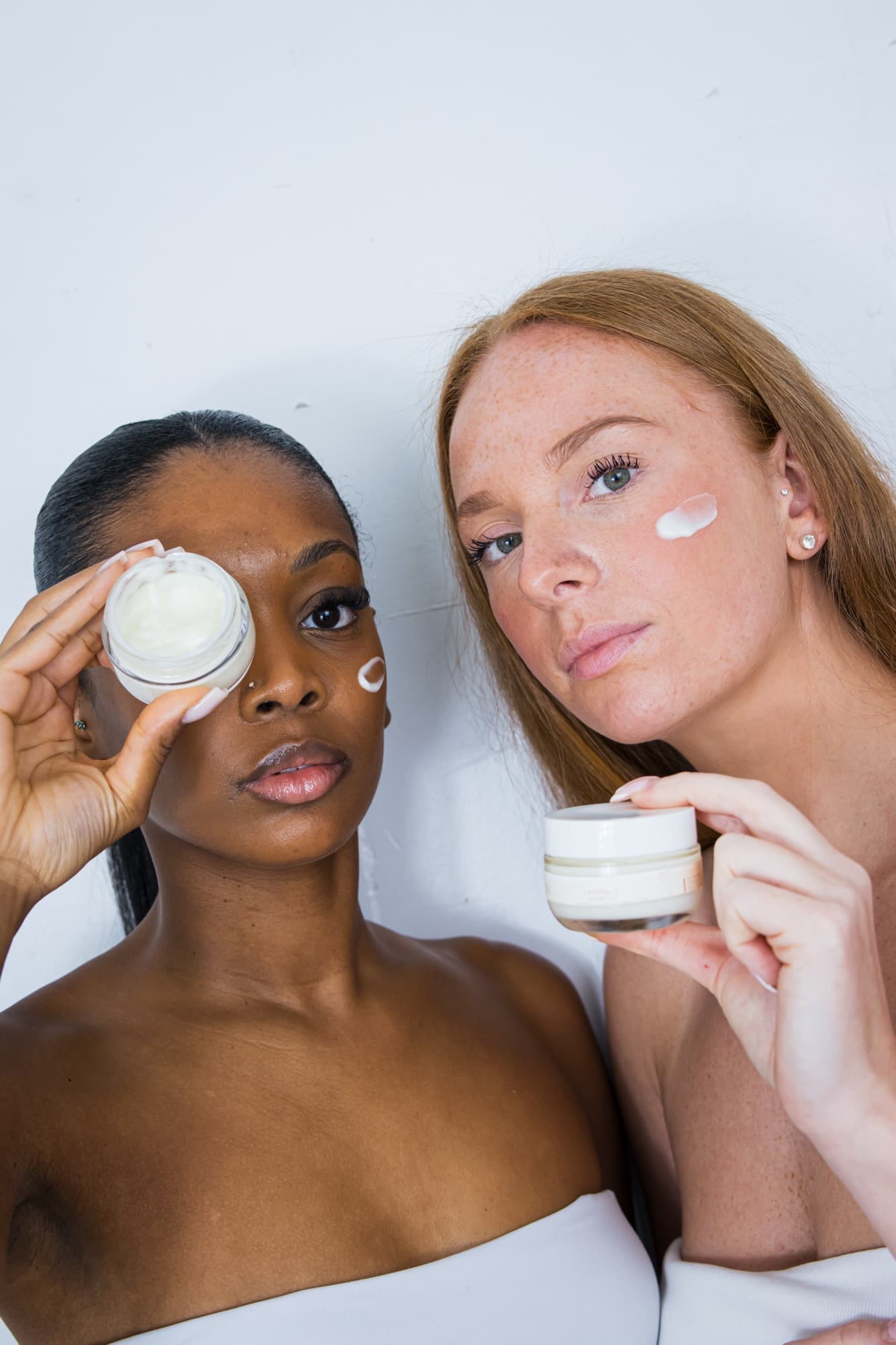 Deux femmes posent avec le pot de crème de nuit Onueï, l’une le tient devant son œil, une trace de crème sur la joue