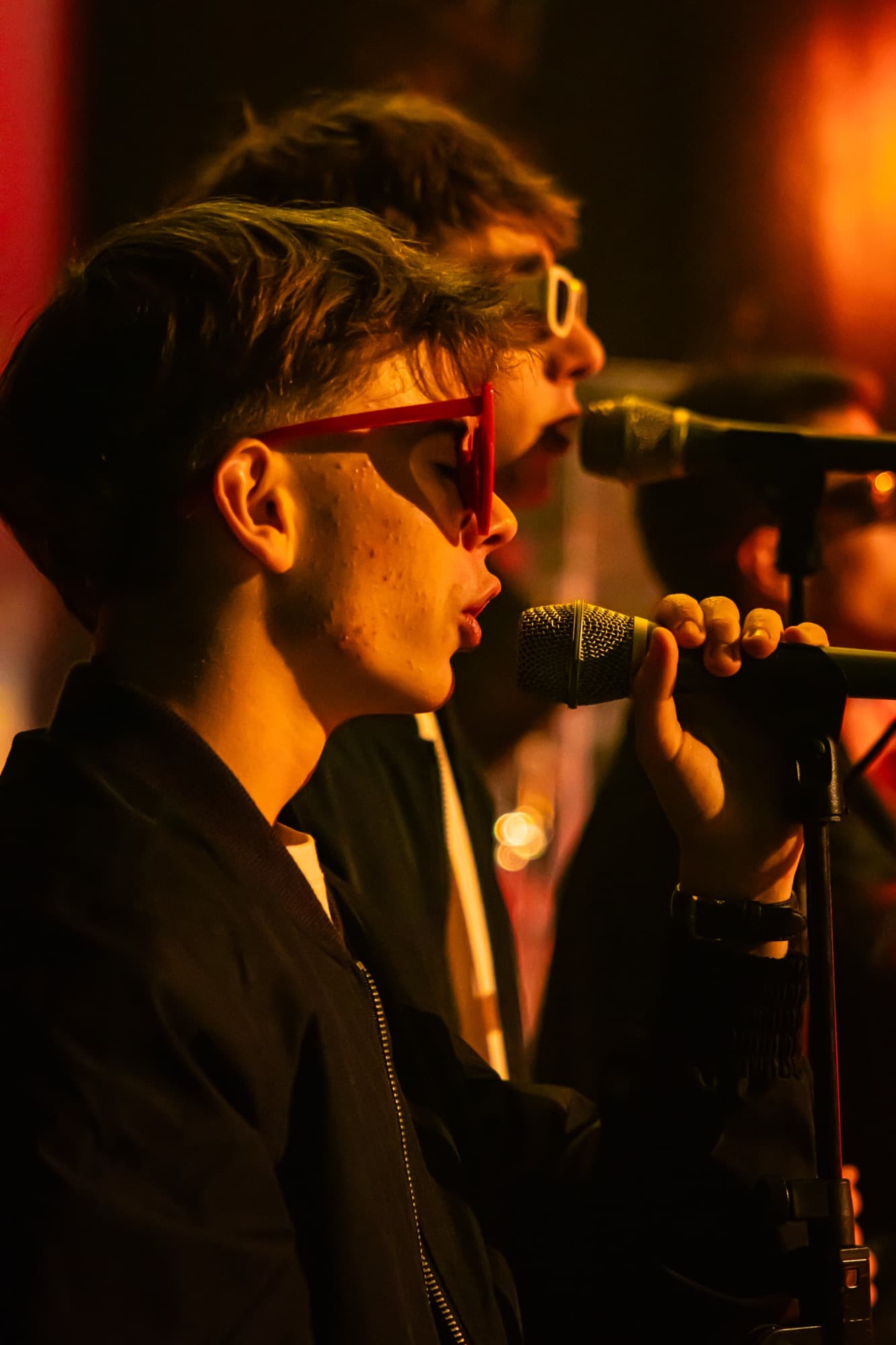 Un chanteur en lunettes rouges au micro, éclairé de lumière chaude