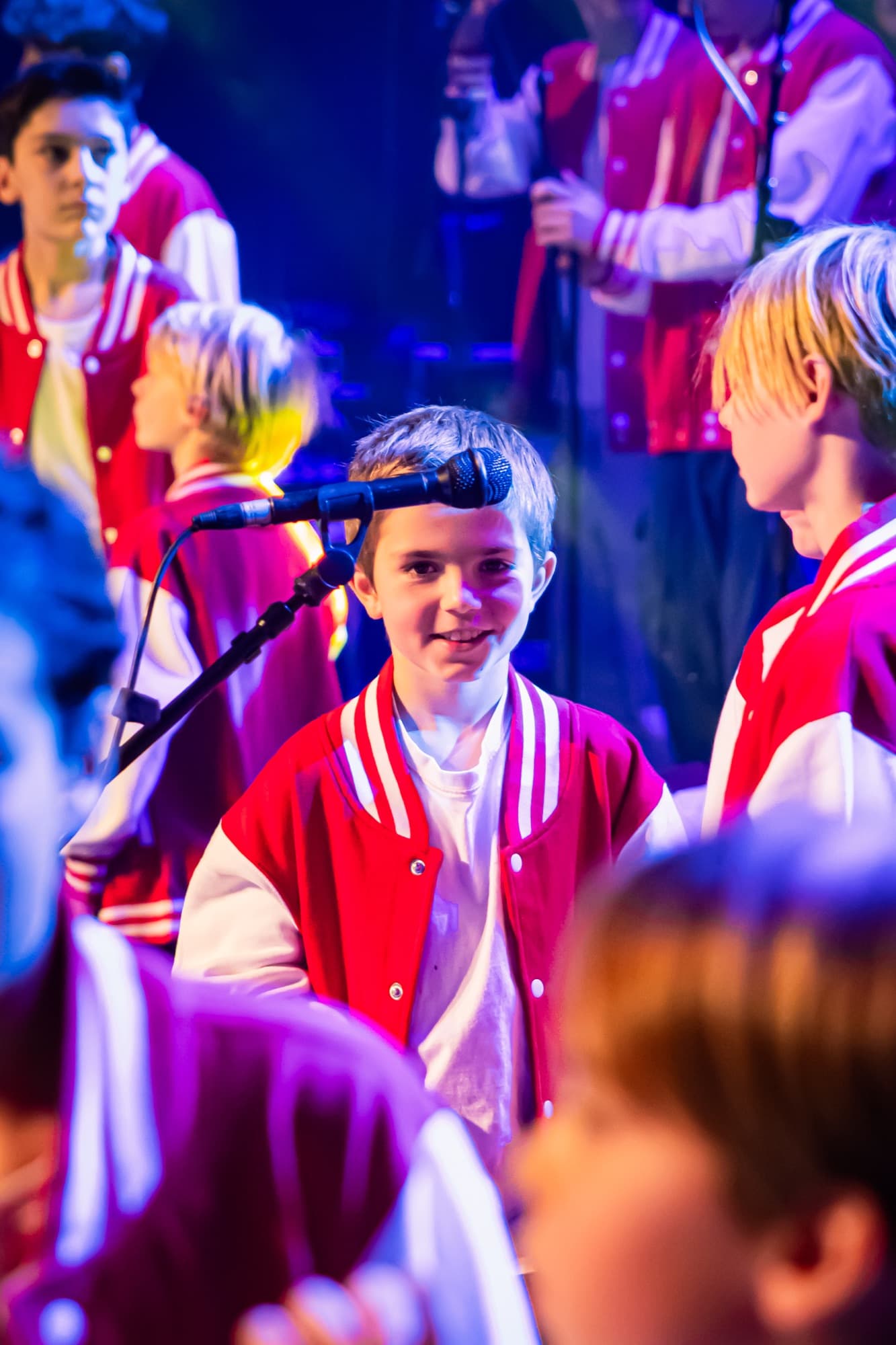 Des choristes en vestes rouges entre deux chansons, sous la lumière bleue de la scène