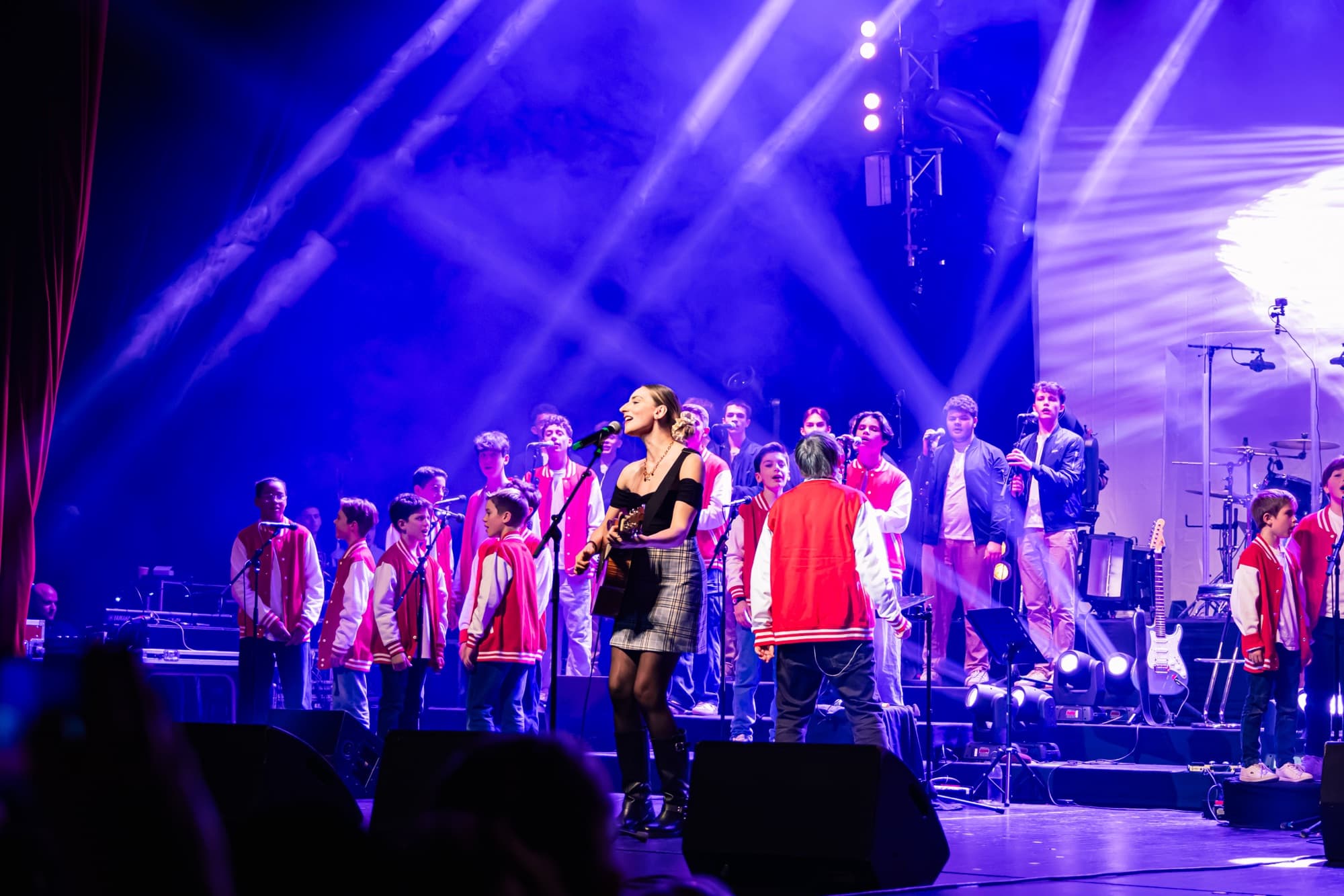 Le chœur en rouge sur scène avec les musiciens, éclairés en bleu