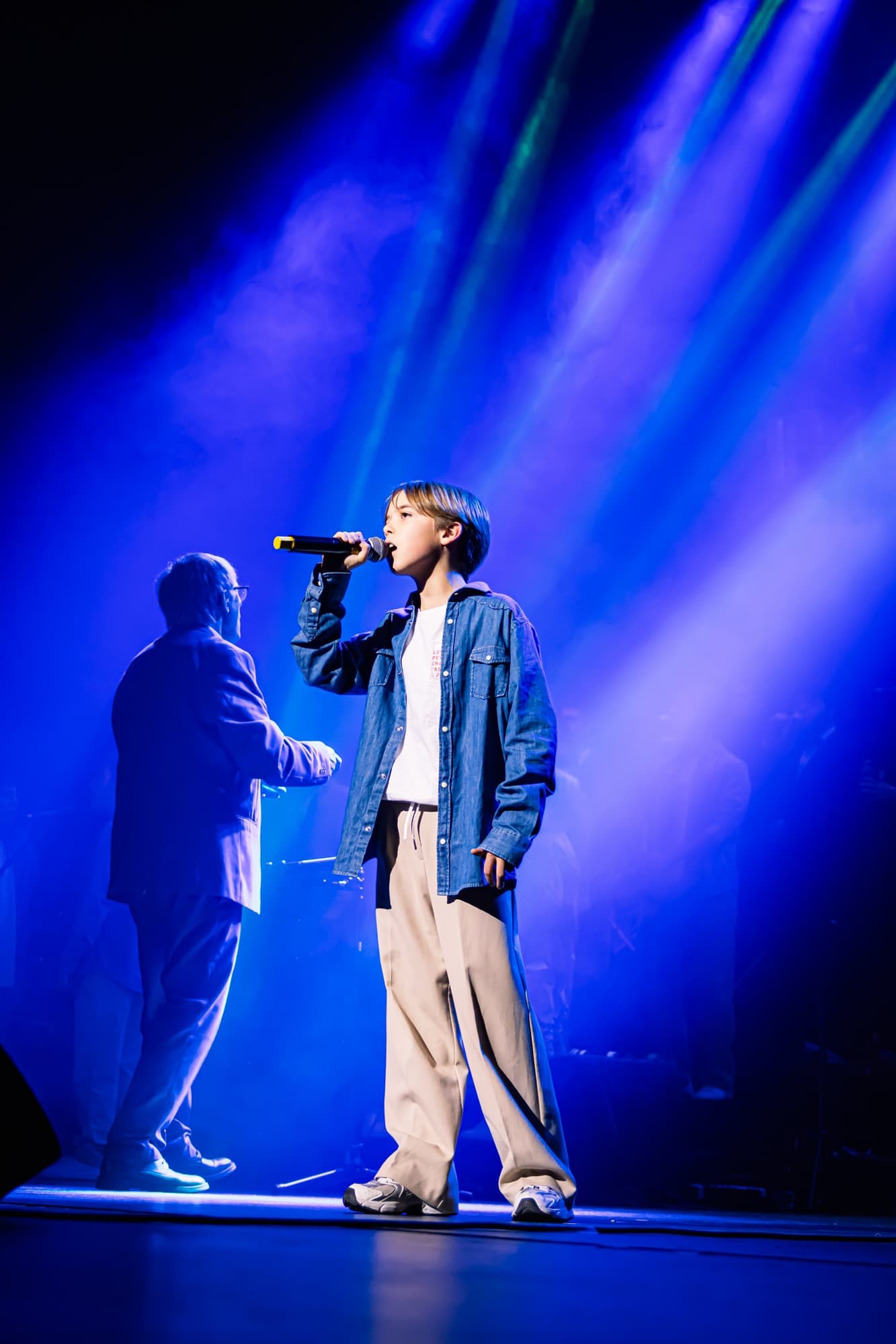 Un chanteur sur scène baigné de lumière bleue pendant le gala des Petits Chanteurs d’Asnières