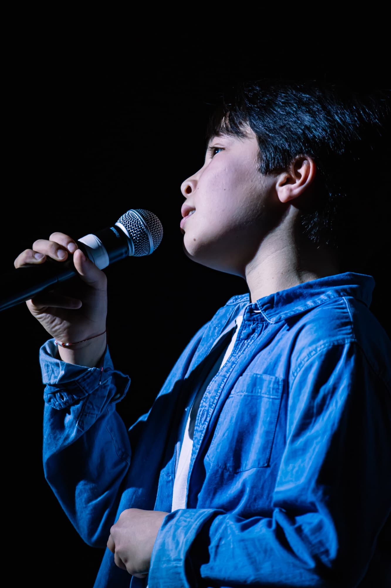 Un jeune soliste chante au micro, de profil, pendant le gala des Petits Chanteurs d’Asnières