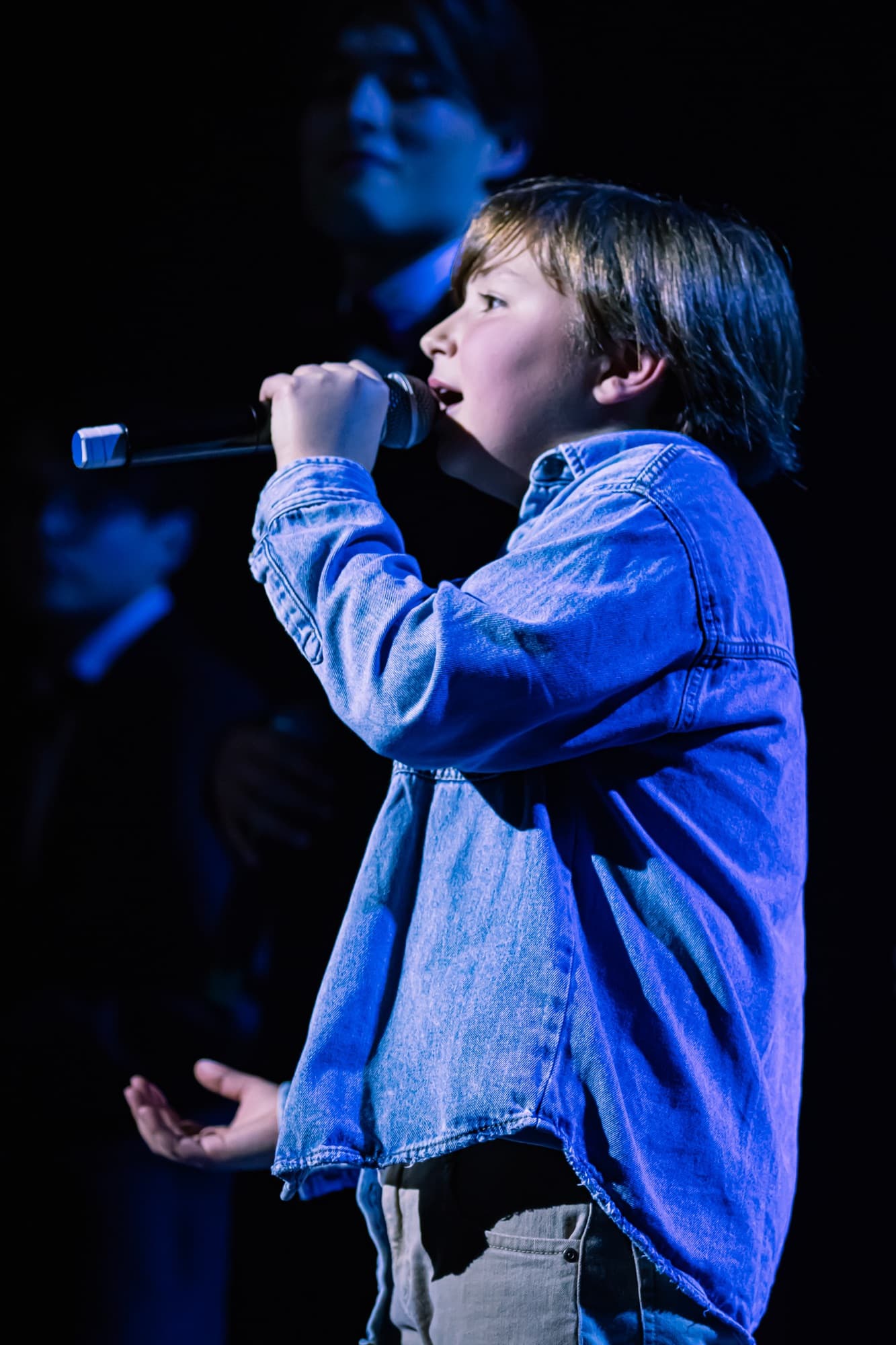 Un jeune chanteur en veste en jean chante dans le micro sur la scène du gala