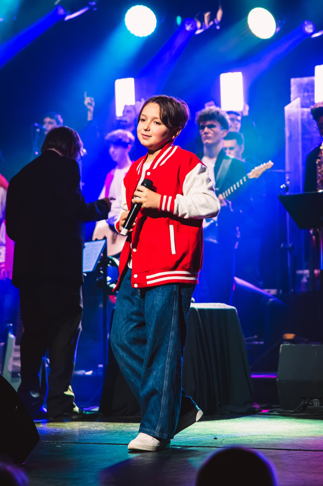 Un jeune en veste rouge devant un guitariste, sur la scène du gala
