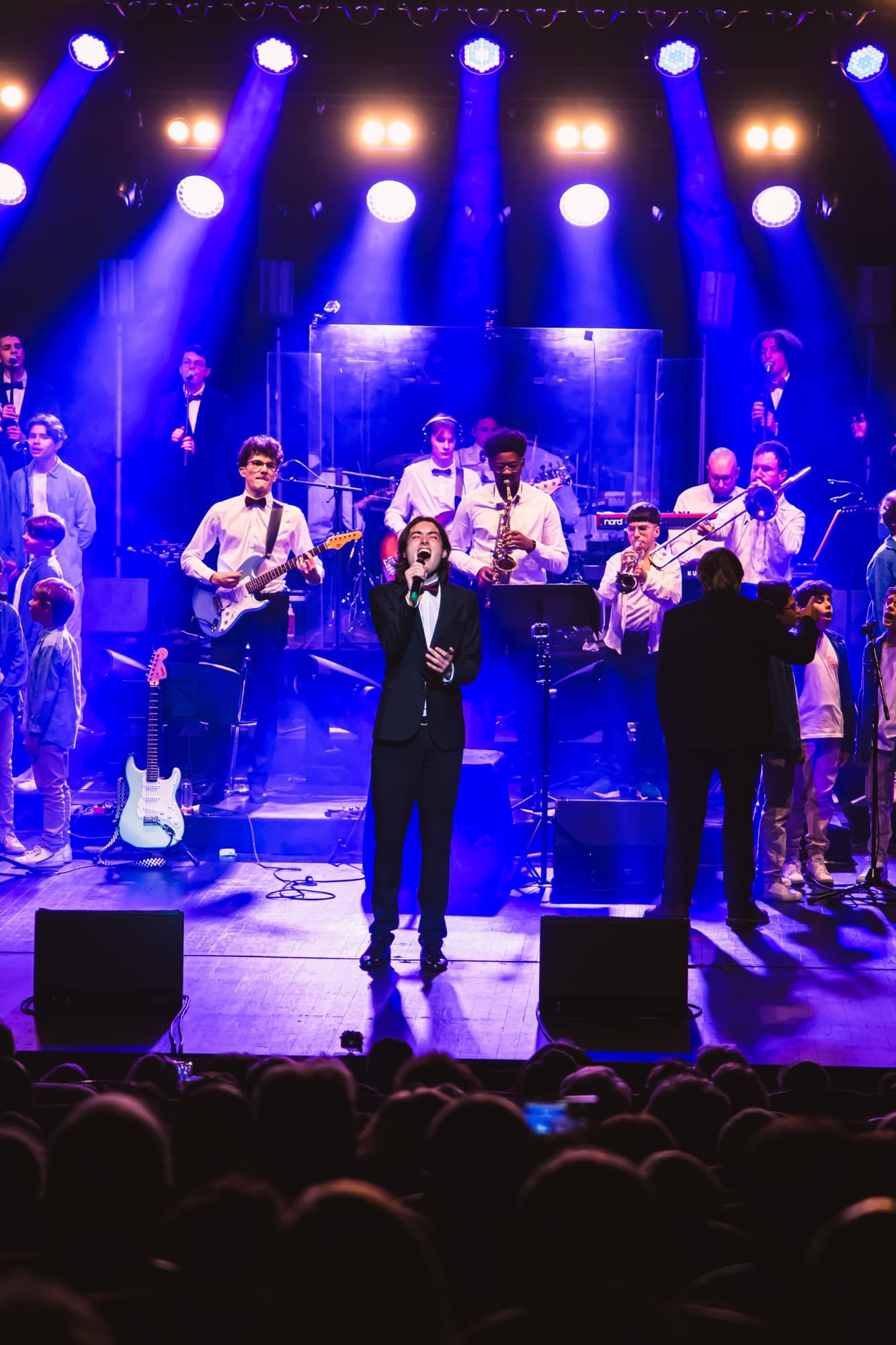 Un chanteur en costume devant le groupe, sur la scène du gala