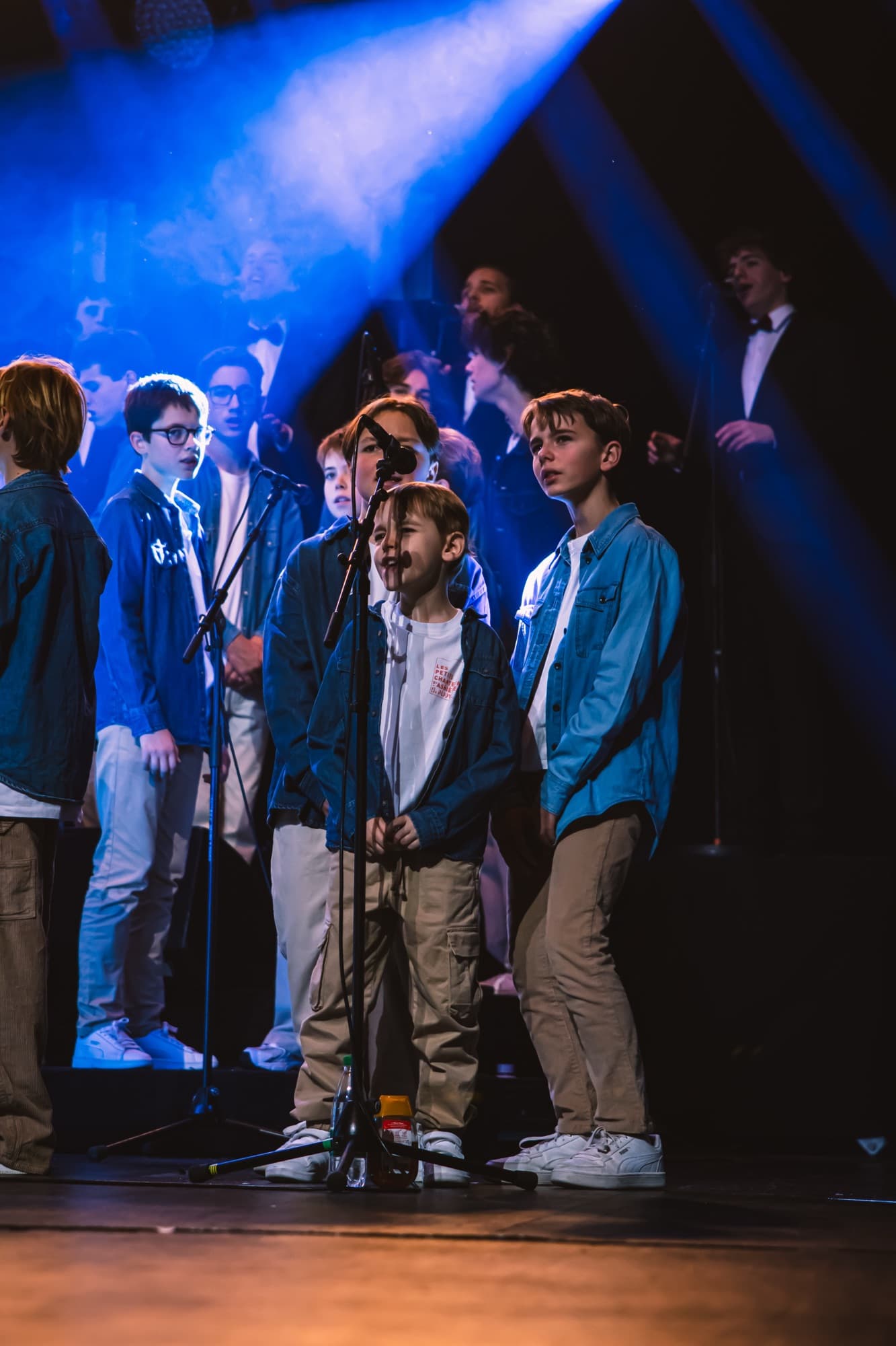Des jeunes choristes en vestes bleues sur scène, sous une lumière bleue