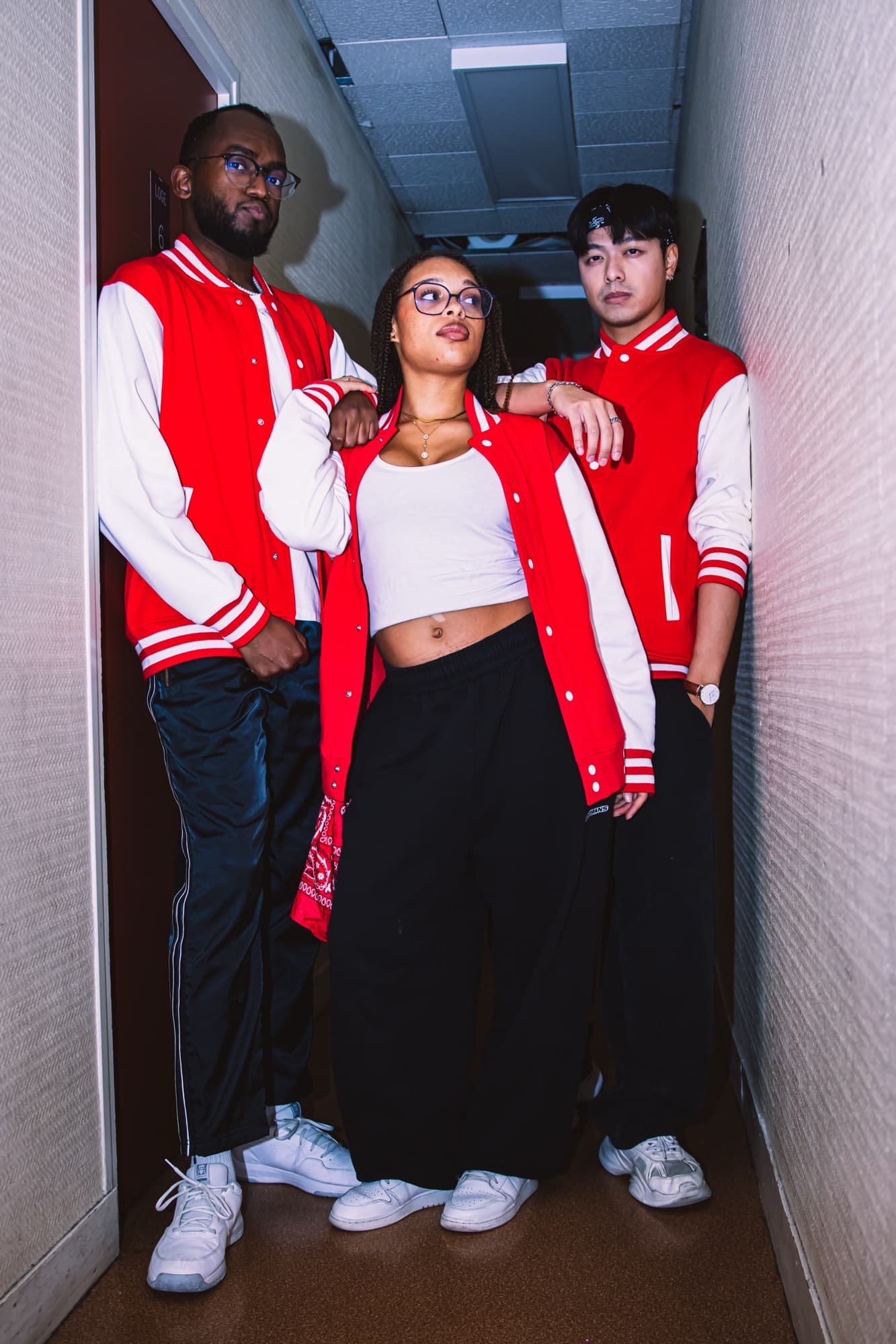 Trois jeunes en vestes rouges posent ensemble dans un couloir
