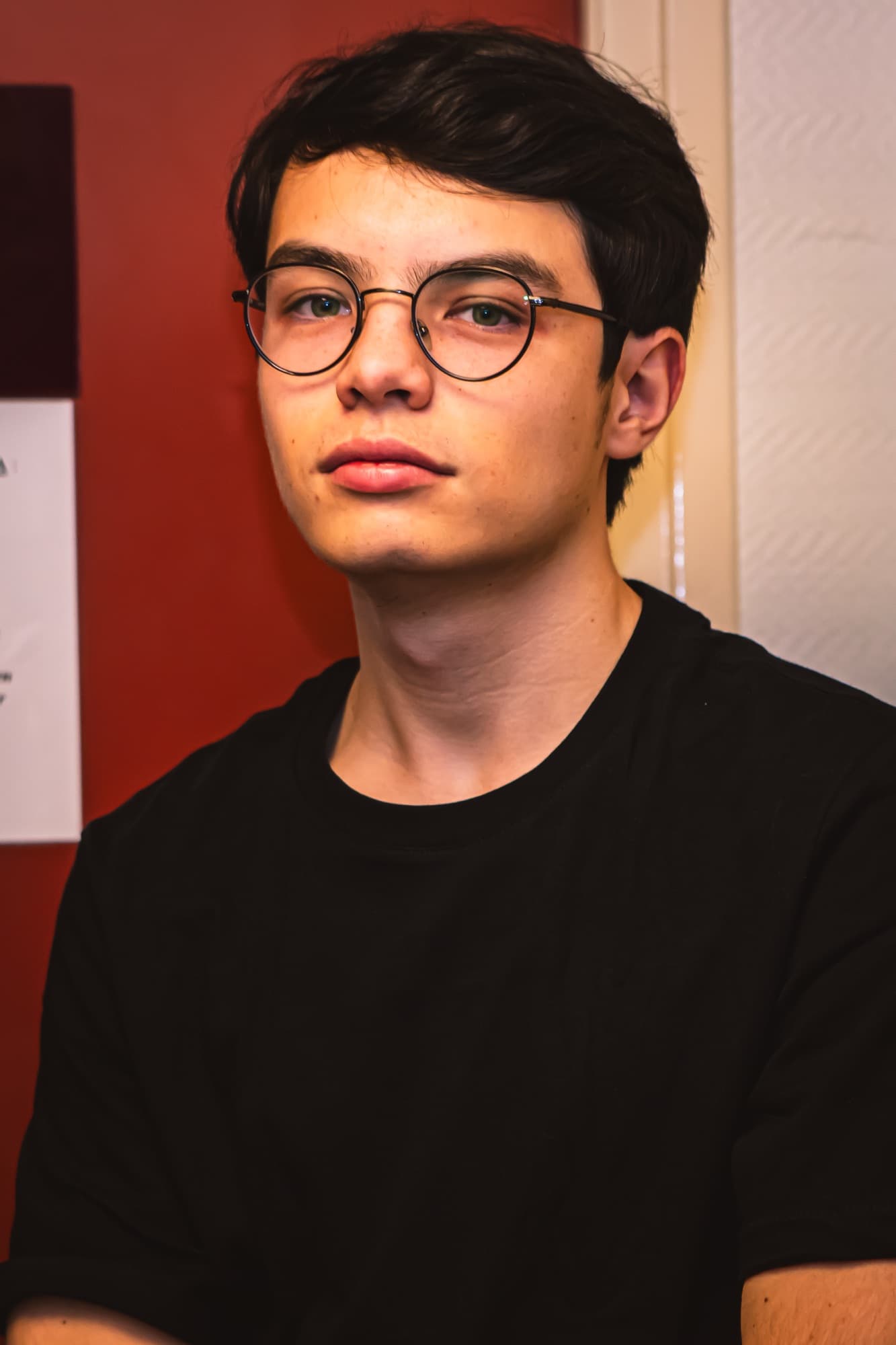 Portrait d’un adolescent à lunettes, sur fond rouge, en coulisses