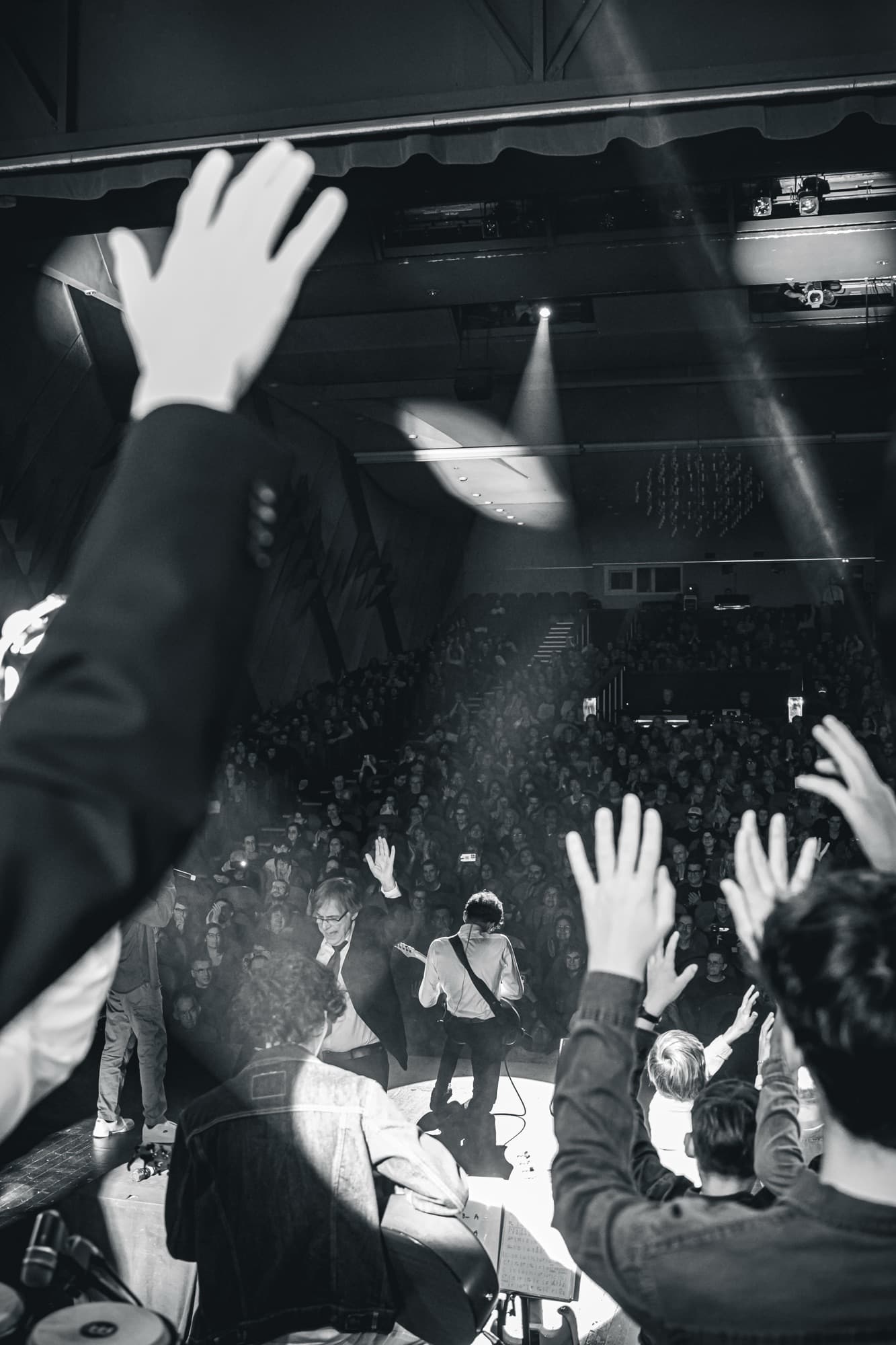 Les mains du public levées dans la salle, en noir et blanc