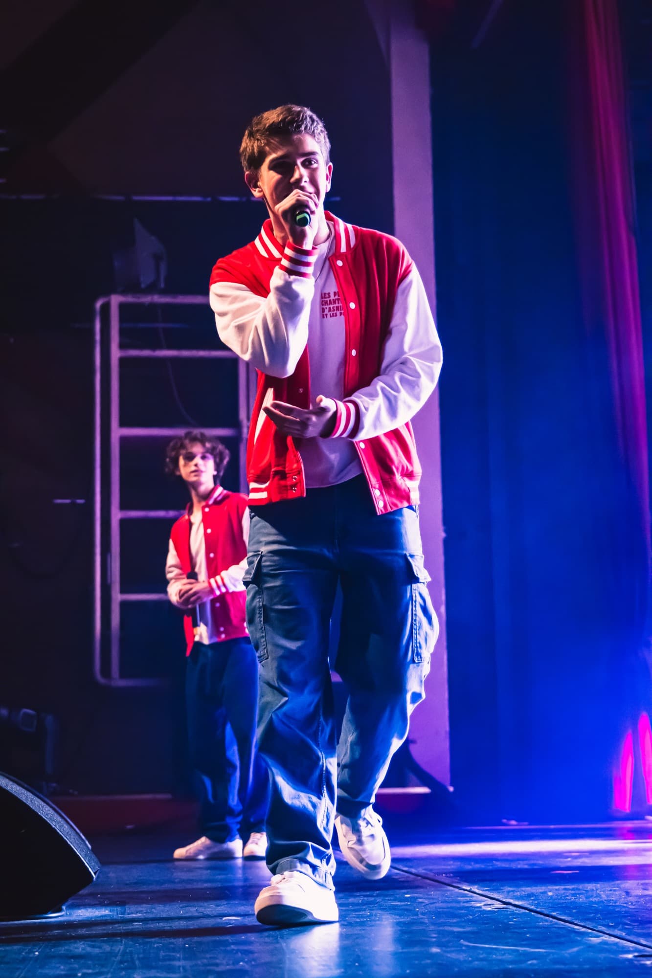 Un jeune soliste en veste rouge chante au micro, sur la scène éclairée de violet
