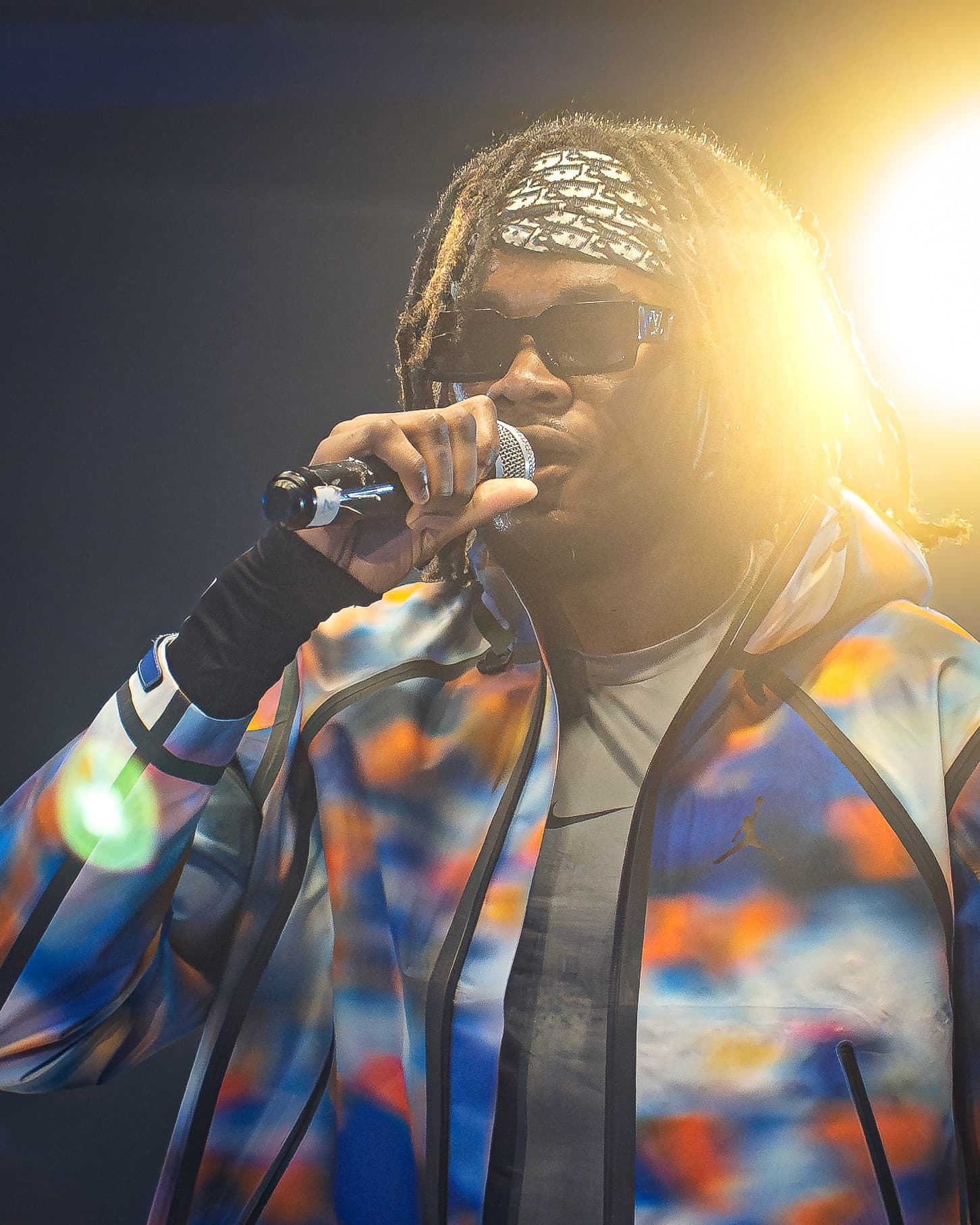 Chanteur au micro, veste multicolore, éclairé à contre-jour
