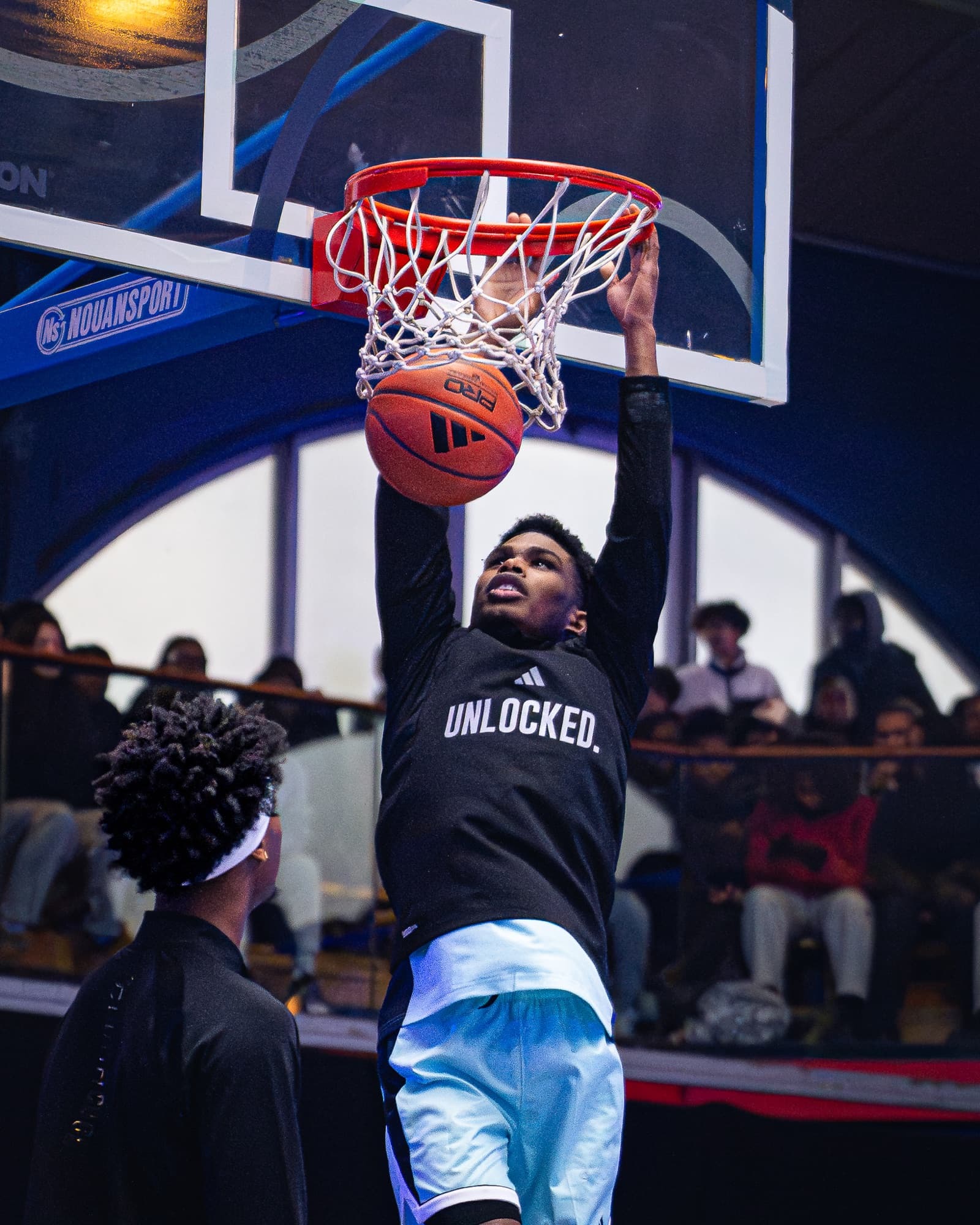 Joueur en plein dunk, ballon au cercle, maillot UNLOCKED, public en tribunes — Unlocked Winter Games 2025