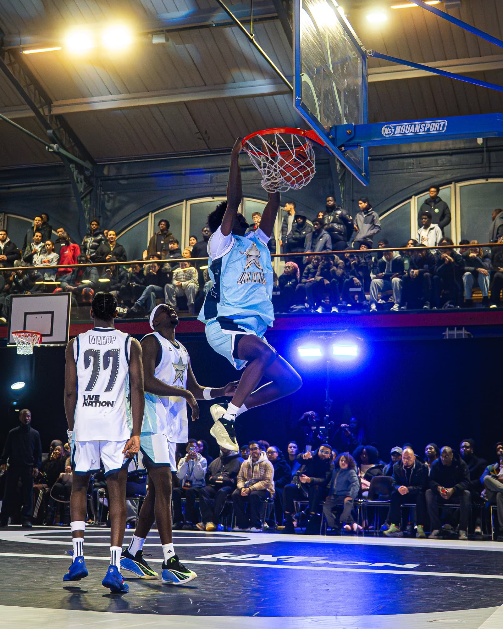 Joueur suspendu au cercle après un dunk, coéquipiers en arrière-plan