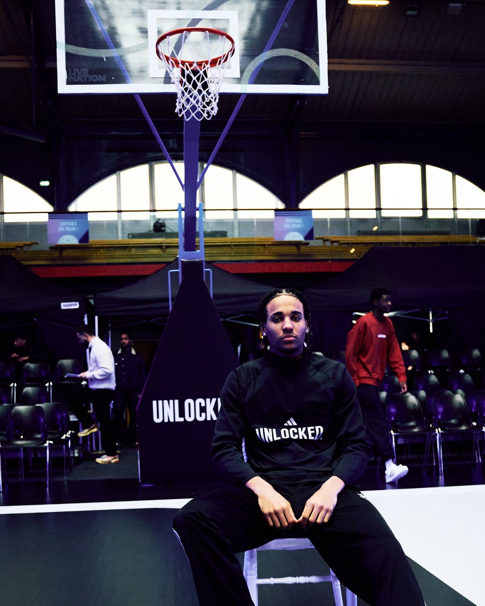 Homme assis au bord du terrain, sweat UNLOCKED, panneau de basket derrière lui