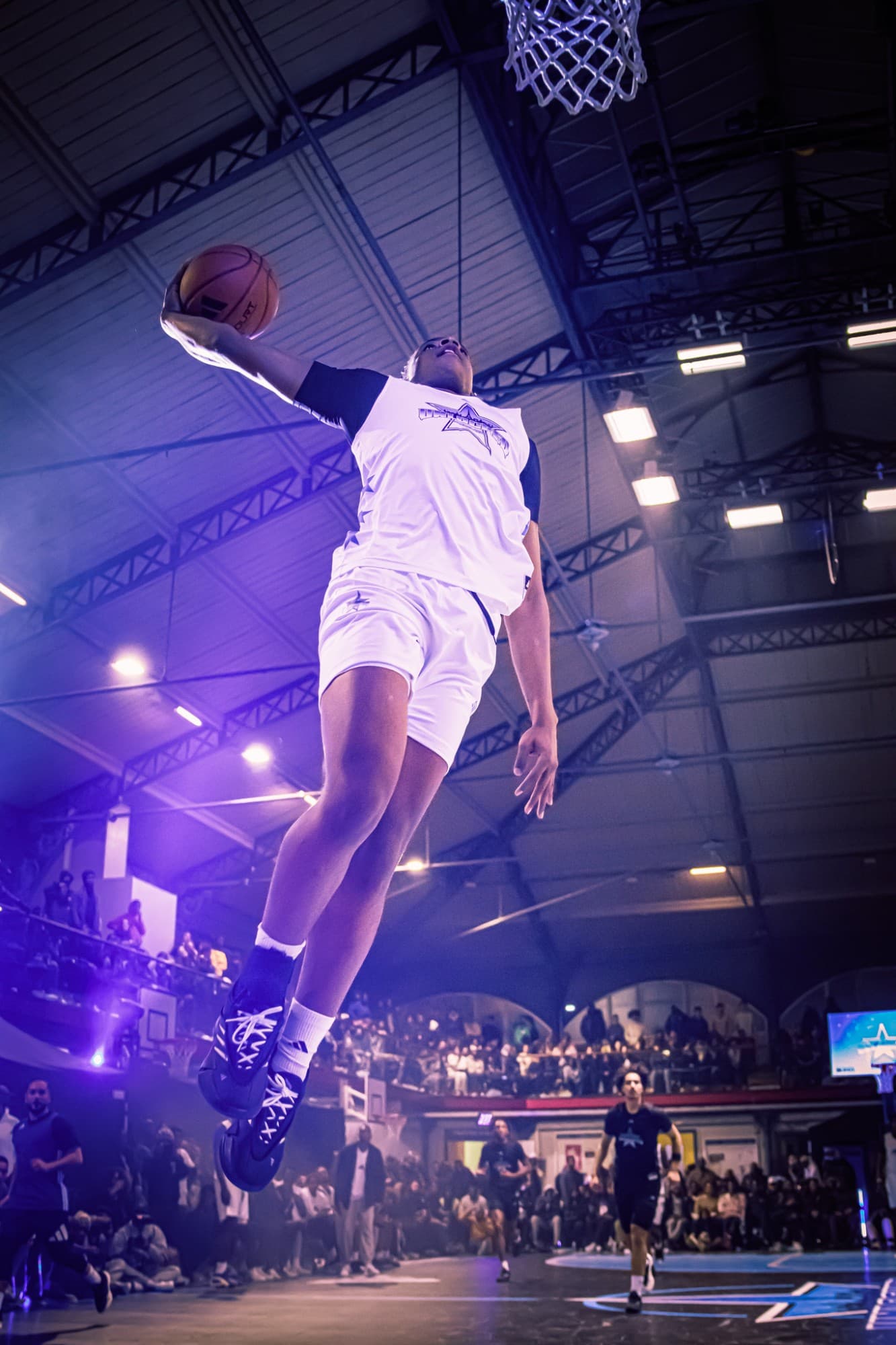 Dunk en contre-plongée dans la salle, public en tribunes