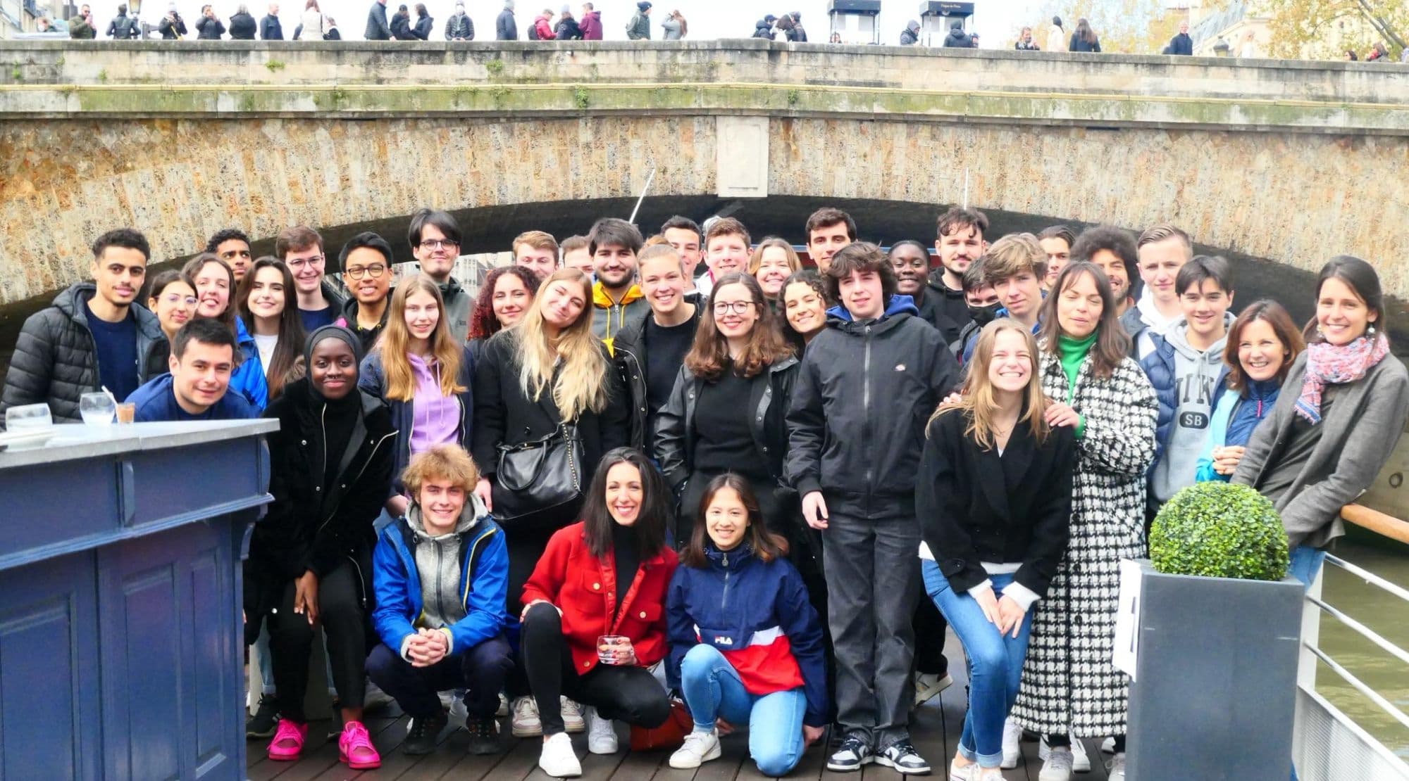 Photo de groupe des jeunes du Youth Council Paris 2024, réunis à bord d’un bateau, sous un pont de Paris